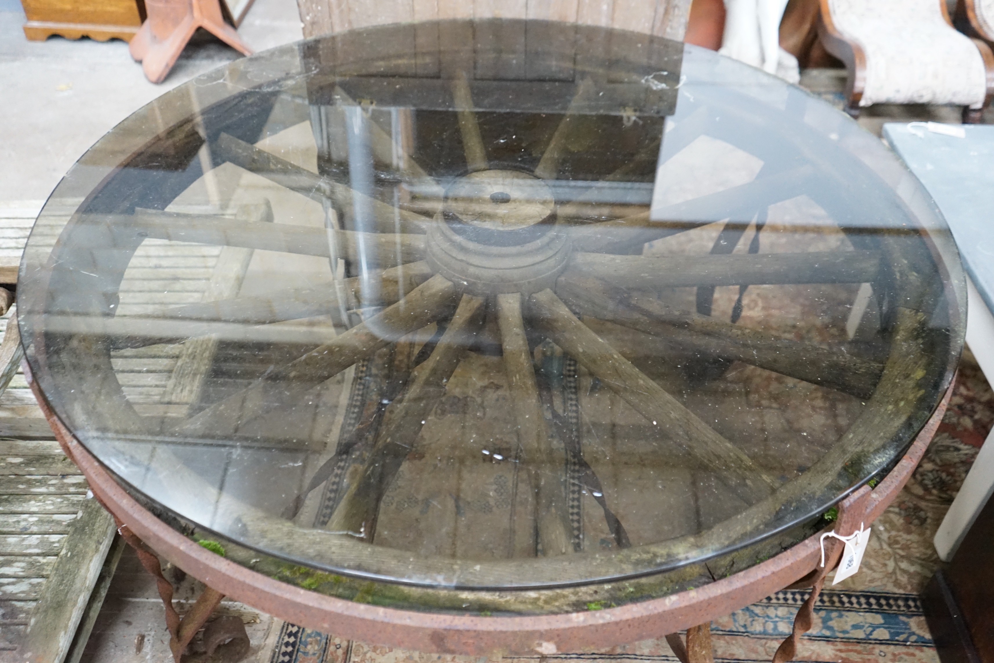 A wrought iron glass topped circular cartwheel garden table, diameter 124cm, height 72cm